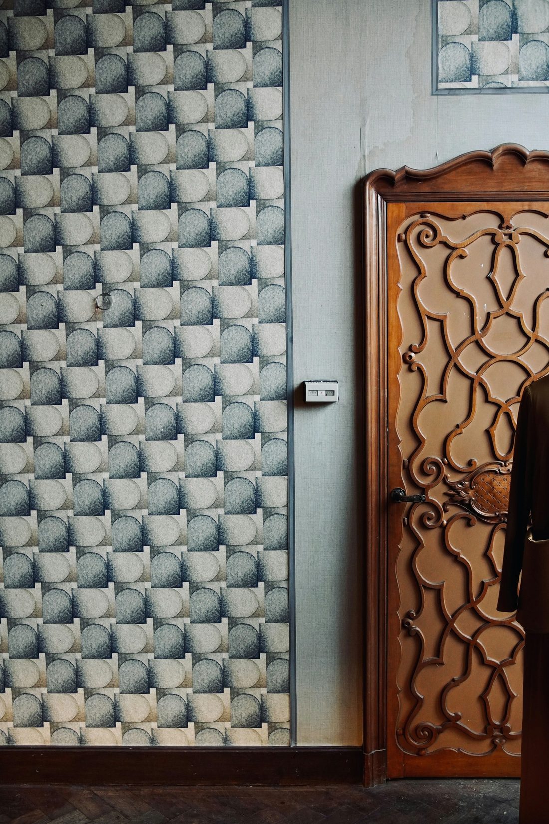 Close view of scalloped fan-pattern wallpaper aligned beside an ornately carved wooden door