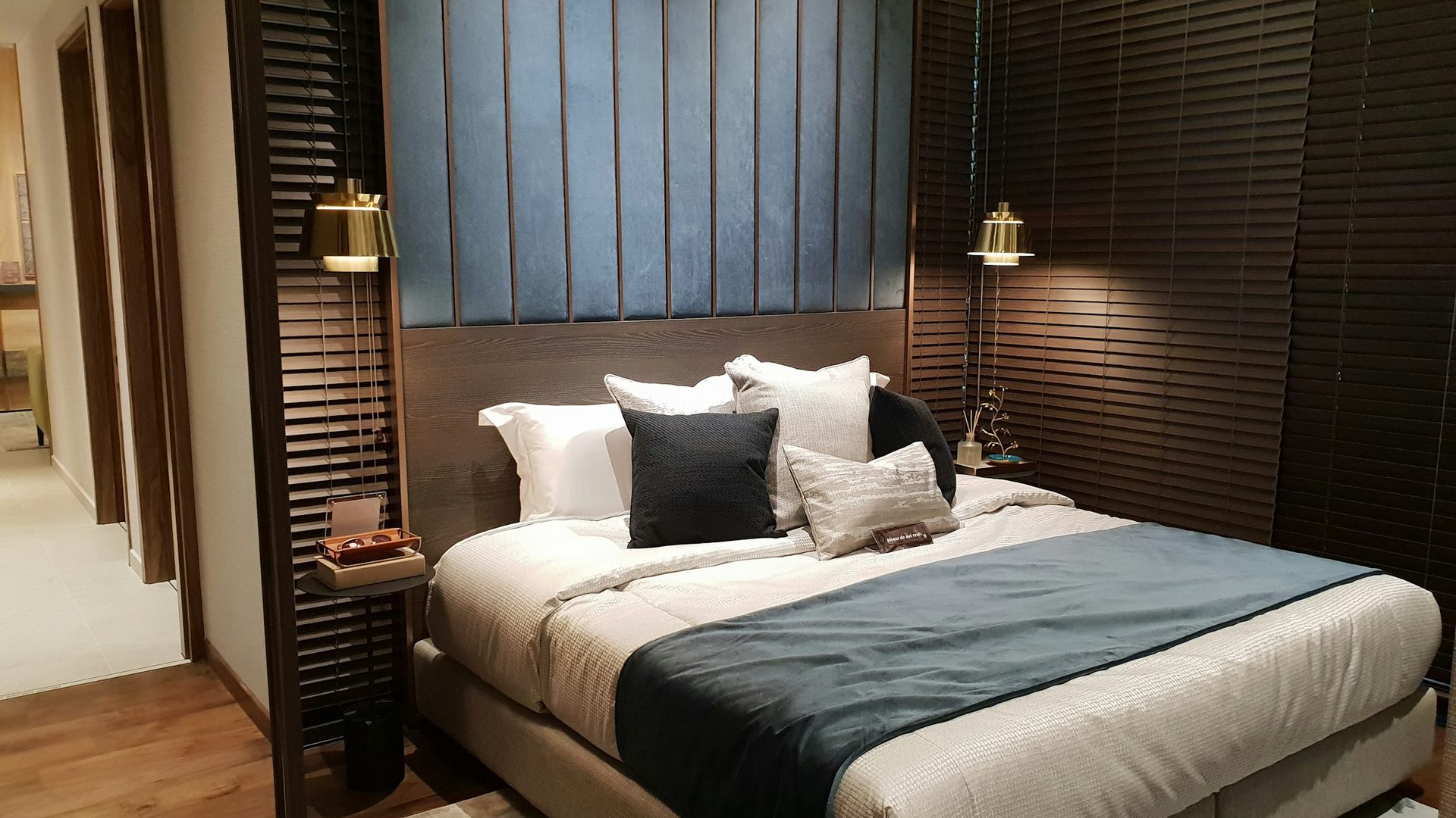 Designed New York bedroom with a deep blue velvet feature wall, warm walnut detailing and brass reading lights