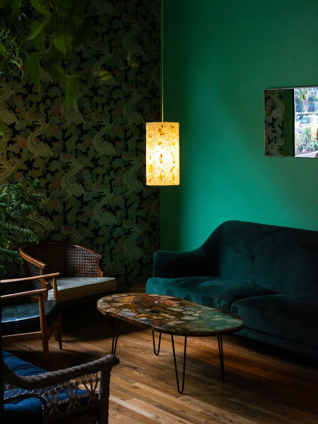 Living room with a deep botanical wallpaper feature wall behind a teal velvet sofa