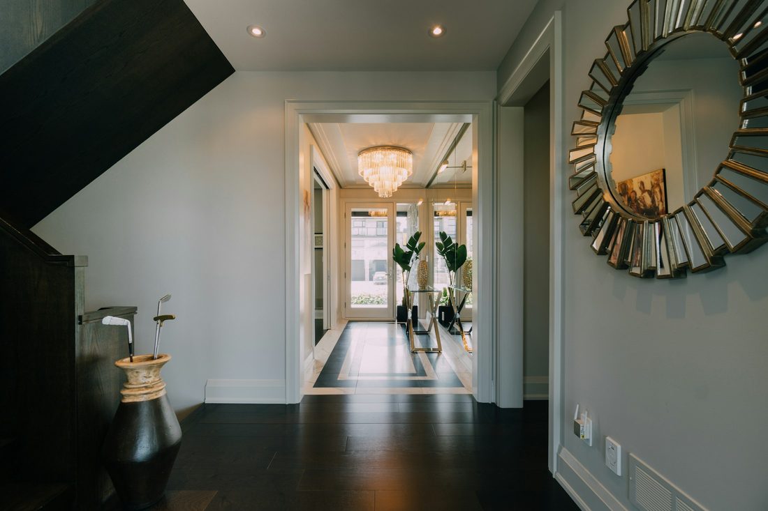 Elegant entryway with a gilded sunburst mirror, sconce lighting and a long bright hallway beyond