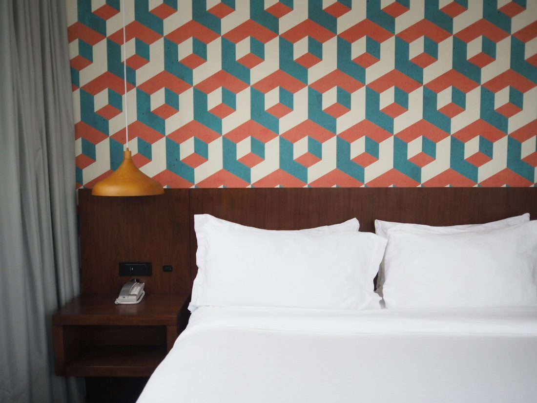 Bedroom accent wall finished with a bold geometric wallpaper above a low wooden headboard